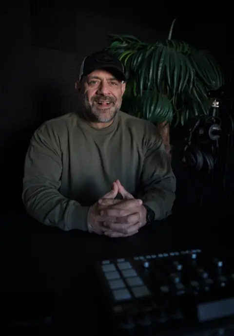 Ashkan Aghili vid inspelningsbordet med mixer och hörlurar i poddstudion