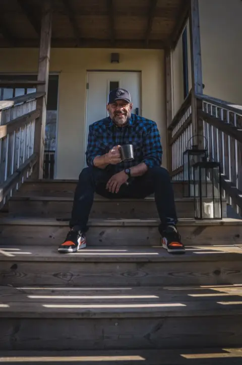 Ashkan Aghili sitter på en trappa utanför ett hus med en kaffekopp i handen