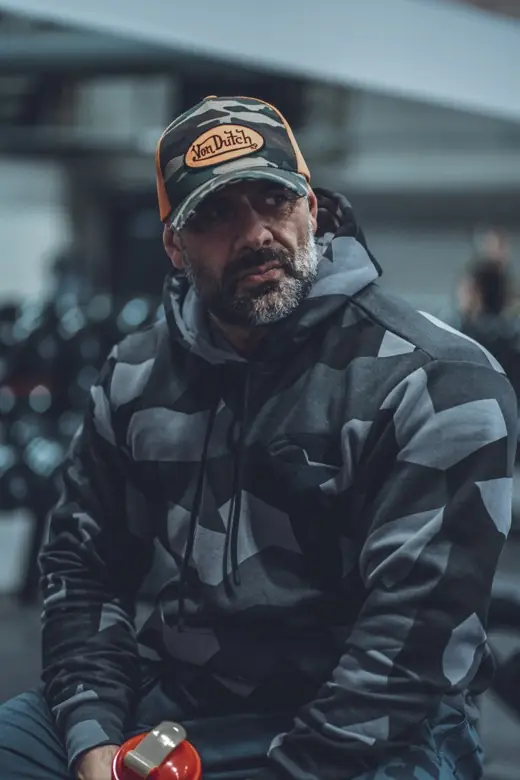 Ashkan Aghili i mönstrad huvtröja och keps på ett gym