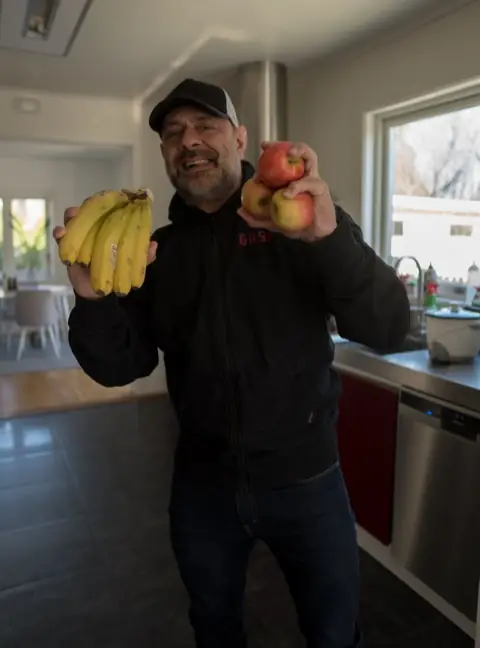 Ashkan Aghili står i ett kök och håller upp bananer och äpplen