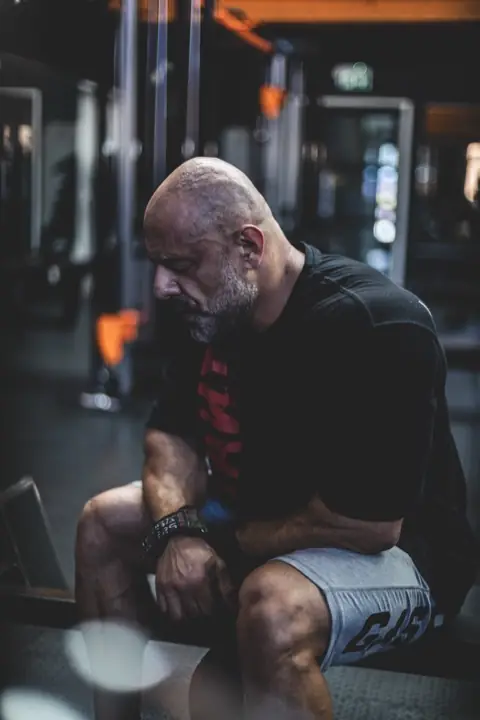 Ashkan Aghili sitter framåtlutad på en bänk och hämtar andan efter ett set